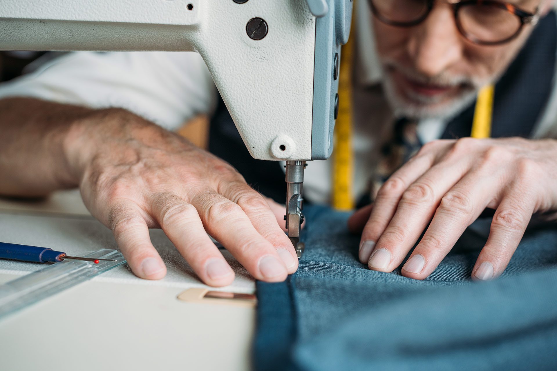 Tailor sewing denim fabric on industrial sewing machine in garment workshop