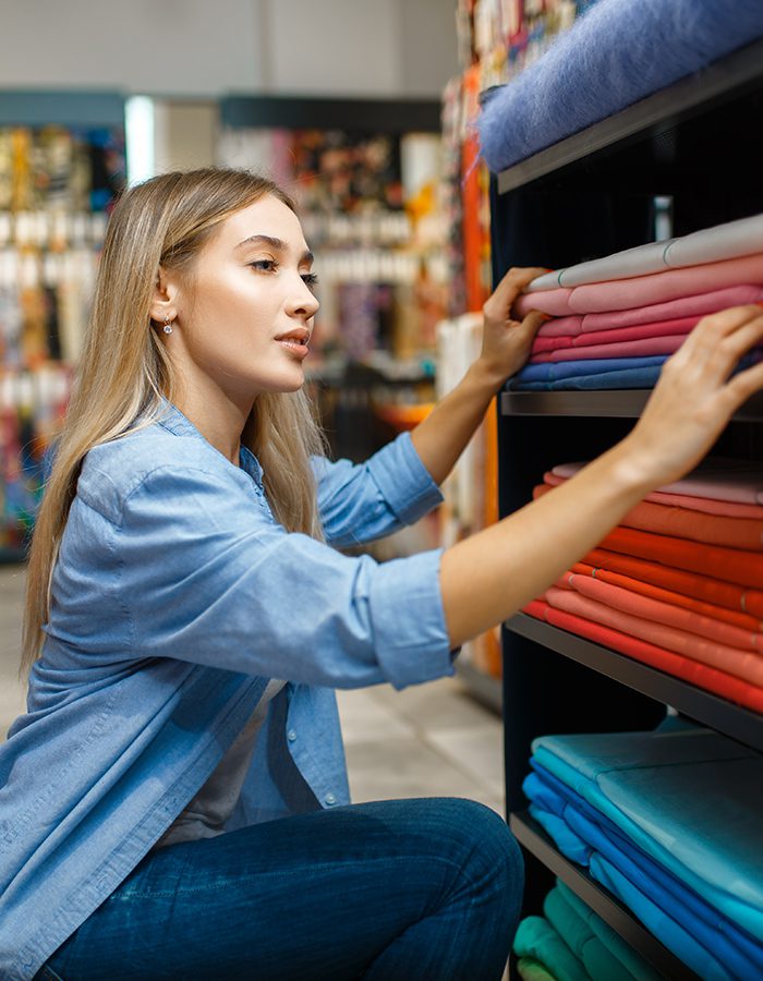 Woman selecting colorful fabric rolls from shelf in textile store ✅ Title
